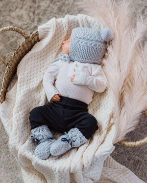 Baby in a basket wearing a white top and navy pants and light blue bonnet and bootie set