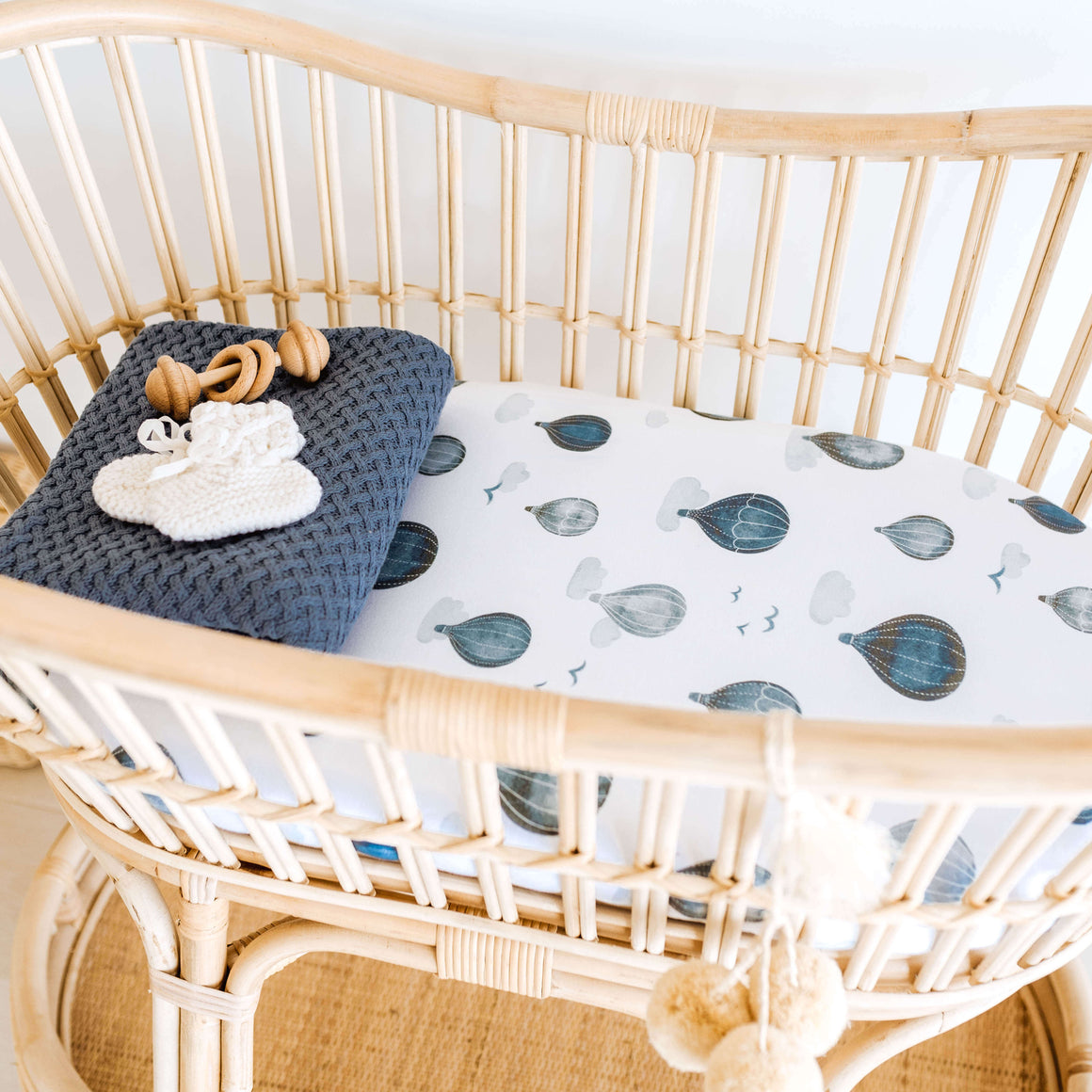Rattan bassinet with cloud and hot air balloon sheet and folded blue blanket