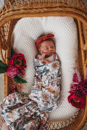 Newborn wearing a deep rust headband and floral swaddle in a basket