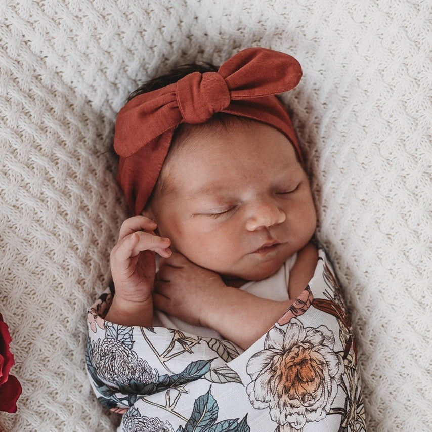 Newborn wearing a deep rust headband and floral swaddle