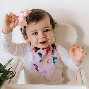 Little girl wearing a floral (white, pink and purple colour) dribble bib and pink bow