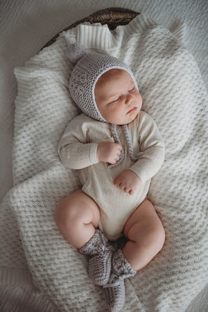 Baby wearing a cream outfit and grey merino wool bonnet and bootie set