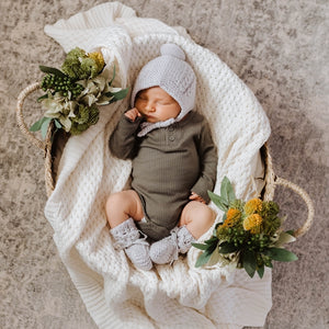Baby in basket wearing a green outfit and grey bonnet and bootie set