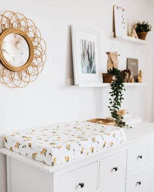 Lemon print change pad cover on white chest of drawers and mirror and pictures on wall