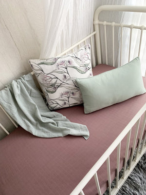 Mauve fitted cot sheet with pillows in a white cot