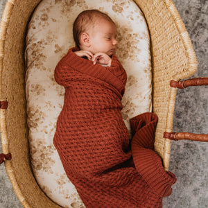 Baby wrapped in rust coloured knit blanket in basket