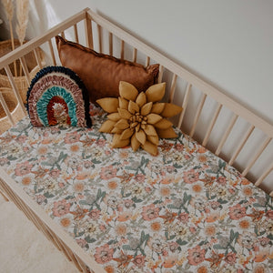Australiana fitted cot sheet, floral pattern with pinks, orange and green colours, three pillows sitting in a wooden cot
