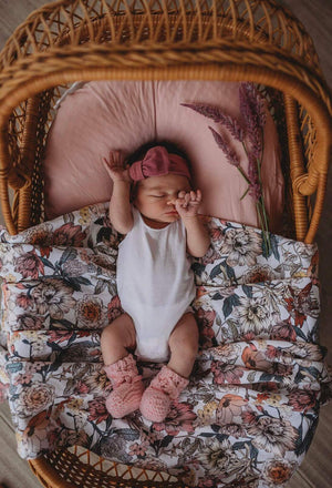 Newborn girl laying on Australiana floral print wrap and wearing a mauve pink bow