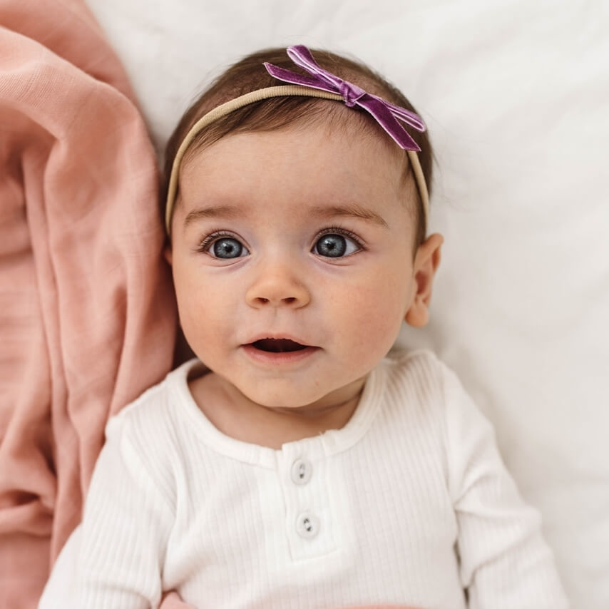 Baby girl wearing a white shirt and grape velvet bow