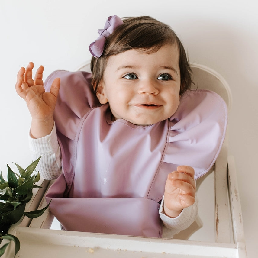 Girl toddler with purple bib on and purple bow in hair
