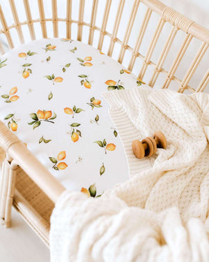 Lemon print bassinet sheet and cream knit blanket in rattan bassinet