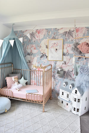 Gold cot with pink cot sheets, three pillows and a doll sitting on cot, floral wall paper in background and green canopy