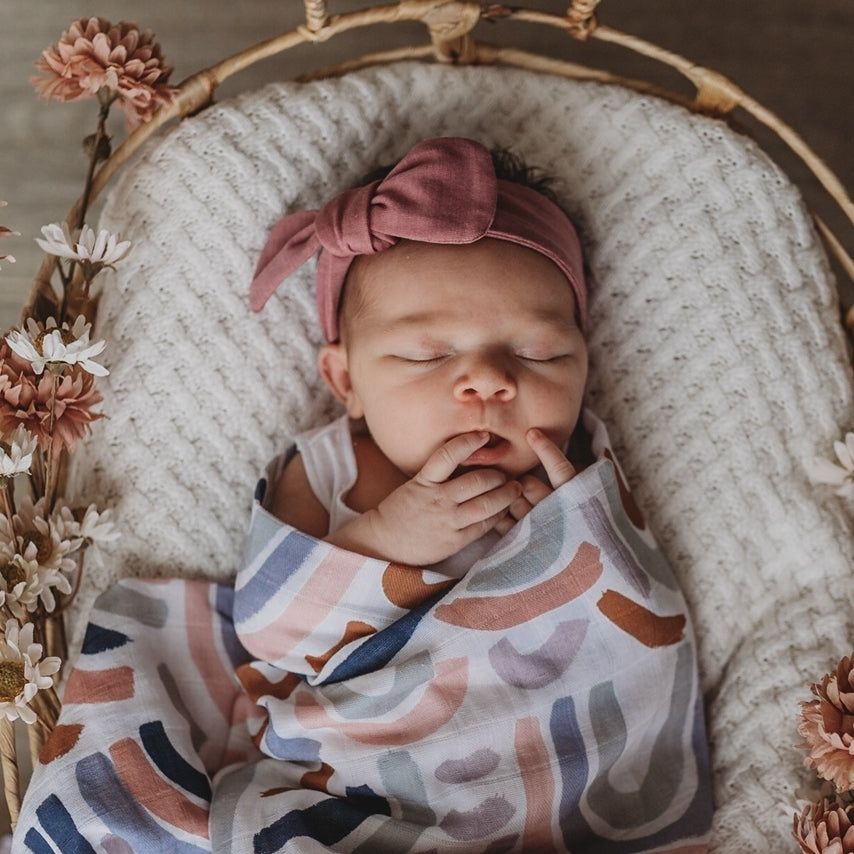 Baby girl in basket wearing a mauve topknot headband and rainbow swaddle
