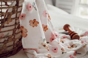 White and pink floral pattern swaddle draped over basket with wooden rattle