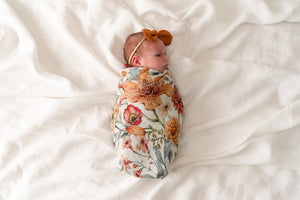 PopYaTo floral muslin swaddle wrapped around a newborn baby girl