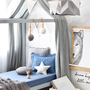 Toddler bed with blue reign cot sheet, pillows and blanket on it, wolf art work on the wall