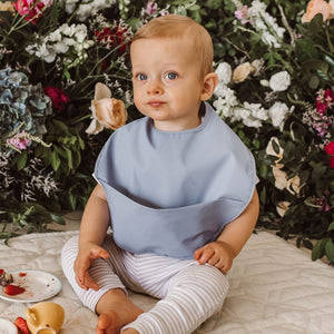 Toddler boy with a light blue bib, flowers in the background