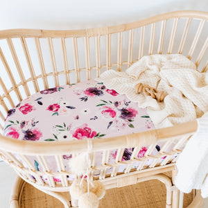 Rattan Bassinet with a floral pink and purple sheet and cream knit blanket