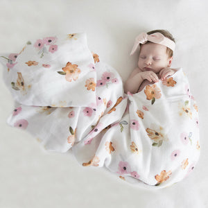 Baby wrapped in a white and pink floral print wrap wearing a bow