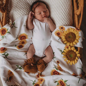 Newborn baby in basket laying on a sunflower print wrap and bow headband on head