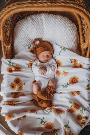 Newborn baby in basket laying on a sunflower print wrap and mustard beanie on head